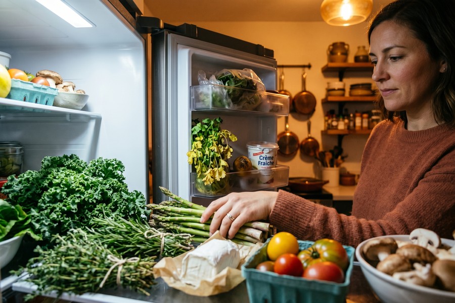 Overflowing fridge full of fresh produce and packaged food, some items starting to go bad