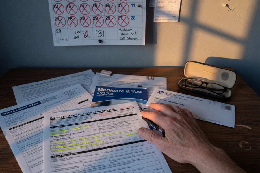Retiree reviewing Medicare plan documents at kitchen table with calculator and paperwork
