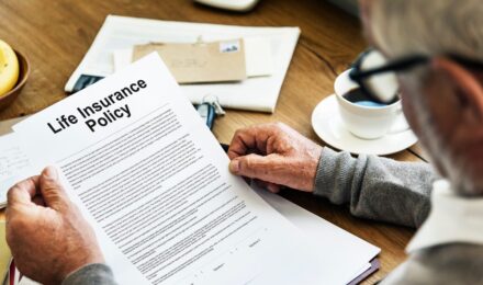 Person reviewing life insurance policy details with a calculator and documents on a desk