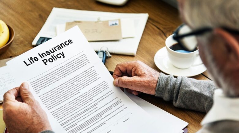 Person reviewing life insurance policy details with a calculator and documents on a desk