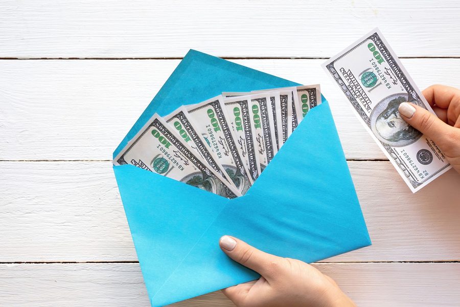 Smartphone displaying a budgeting app beside a traditional cash-filled envelope on a wooden table
